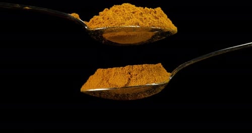 Spoon and Curry Powder falling against Black Background, Slow motion 4K