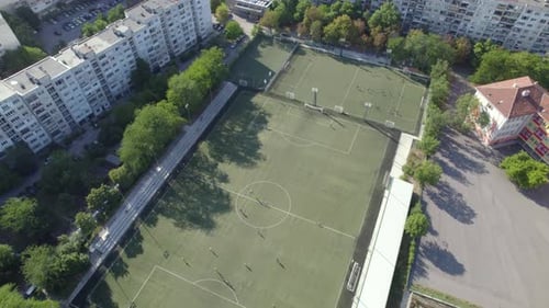 Aerial Shot of a City with a Soccer Field and Living Houses with Tall Trees