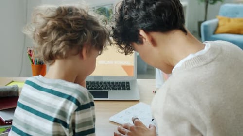 Mother Helping Smart Kid with Studying Writing and Looking at Laptop with Online School Content in
