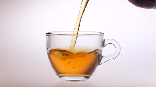 Pouring hot refreshing tea into a glass cup