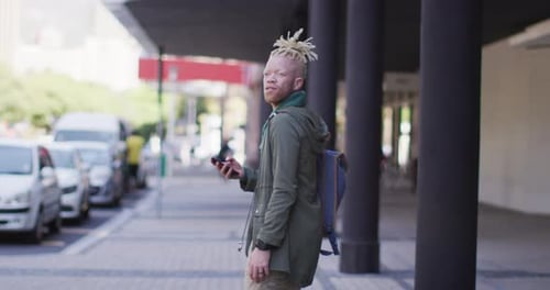 Thoughtful albino african american man with dreadlocks walking on street using smartphone