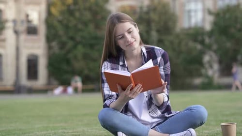 Junge Frau sitzt auf dem Gras und liest Buch