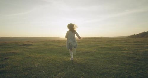 A Little Girl Is Running Through the Autumn Field Against the Background of the Sun