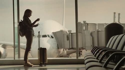 A Woman with a Passport and a Boarding Pass Is Standing at a Large Window at the Airport