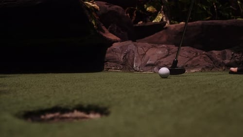 A Young Woman Playing Mini Golf. Legs in the Frame. Mid Shot. Shoot Ball in the Hole
