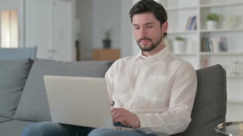 Man Smiles While Working on Laptop at Home
