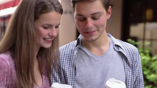 Glückliches Paar benutzt Handy und trinkt Kaffee im Freien