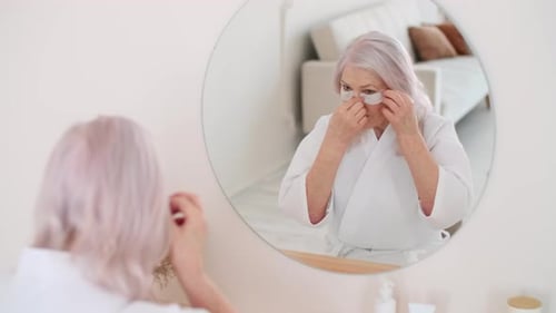 Woman Applies Under-Eye Patches at Her Bathroom Mirror