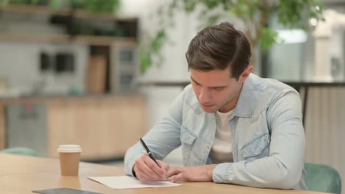 Young Adult Writing on Paper at Desk