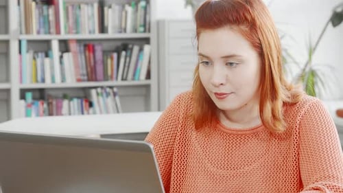 Junge Frau arbeitet an ihrem Laptop in der Bibliothek