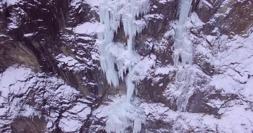 Aerial drone view of a man ice climbing on a frozen waterfall in the mountains.