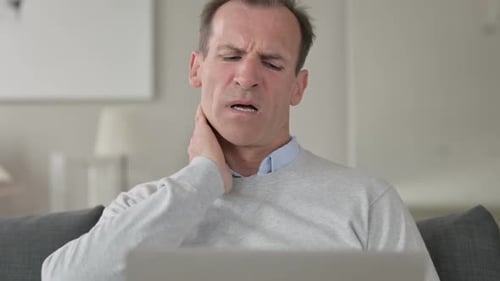 Man Rubs Neck in Pain While Using Laptop