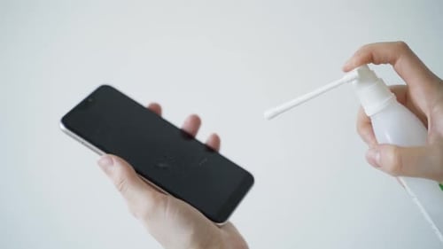 Hand Sprays Cleaner on Smartphone Screen