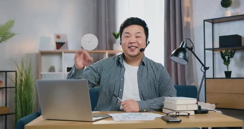 Hombre con auriculares mirando a la cámara en la oficina en casa y mostrando un gesto de acuerdo