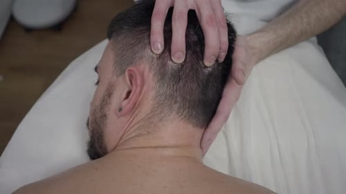 Homem caucasiano barbudo deitado de bruços na cama de massagem como massagista massageando a cabeça