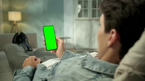 Close Up View of Man at Modern Room Lying on a Sofa Using Phone With Green Mock-up Screen Chroma Key