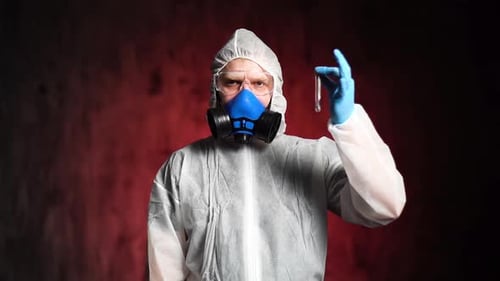 Un científico con traje protector, gafas y respirador sostiene un tubo de ensayo.