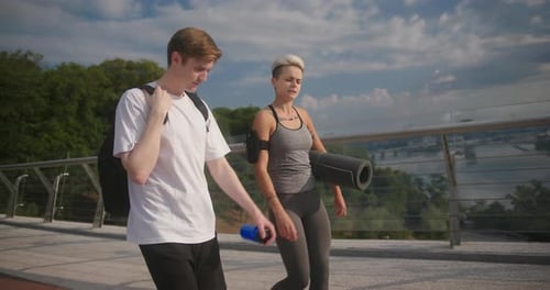 Couple of Young Athletes Walks Along Bridge and Chats