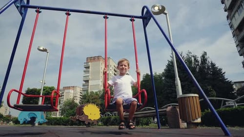 A Boy Swings on a Swing in the City
