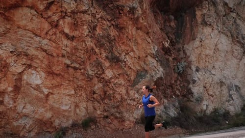 Woman running fast along rocky mountain cliff.