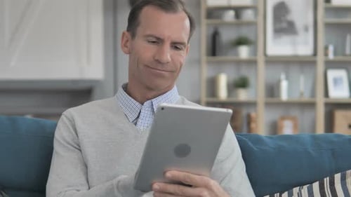 Man Uses Tablet Relaxing on Sofa at Home