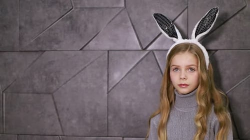 Smiling Girl Wearing Bunny Ears Against Grey Wall