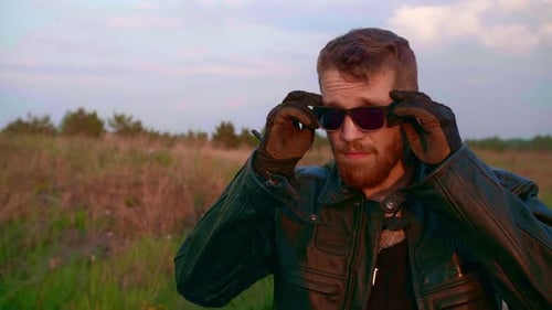 Man with Beard Puts on Sunglasses in Field