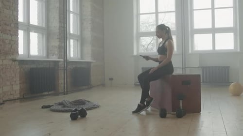 Athletic Woman Uses Smartphone While Resting in Gym
