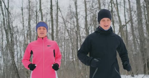 A Man and a Woman in a Pink Jacket in the Winter Running Through the Park