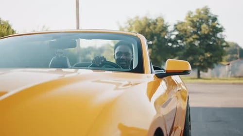 Happy African Man Sitting Inside His New Luxury Yellow Cabriolet Car While