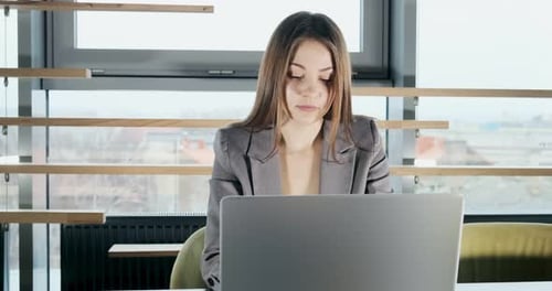 Concerned Woman Working on Laptop Computer and Looking Away Thinking Solving Problem at Office