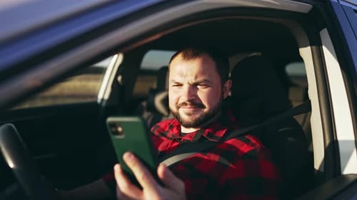 Man Looks at Smartphone in Car Driver's Seat
