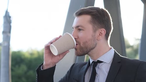 Handsome Businessman in Formal Wear Holding a Cup of Coffee While Looking to the Side