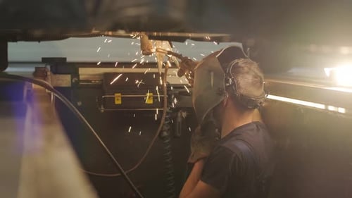 Car service worker welds and repairs an exhaust pipe of a car. Close-up welding