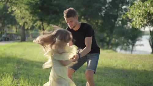 Playful Girl in Yellow Dress Having Fun with Young Smiling Man in Sunny Park