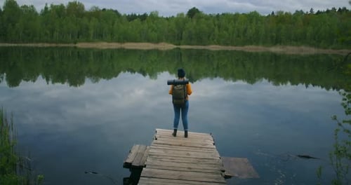 Back View: A Female Traveler with a Backpack Enjoys the Beauty of a Mountain Forest Lake