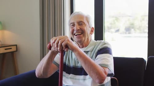Smiling Senior Man Sitting with Cane in Living Room