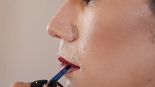 Makeup Studio - Maskenbildner trägt roten Lippenstift über den Stift auf die Lippen eines männlichen Models auf