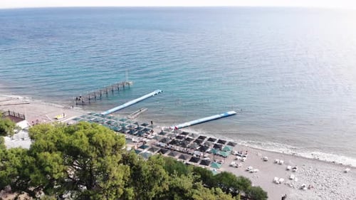 Drone Shooting of the Calm Surface of the Blue Sea and Rows of Sun Loungers on the Shore of a White