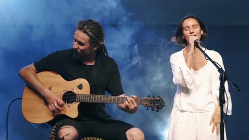 Man Plays Guitar as Woman Sings on Stage