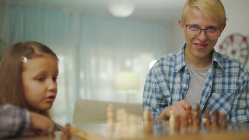 Young Man In Glasses Plays Chess With His Sister Girl At Home