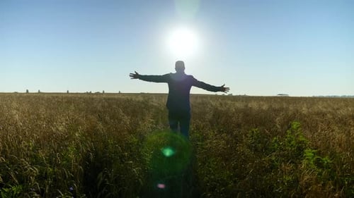 Farmer Businessman with Raised Hands Walks Through the Wheat Field at Sunrise