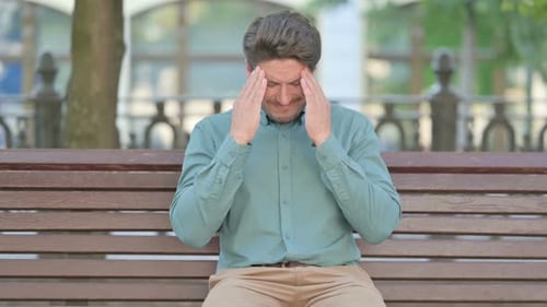 Man Massaging Temples on Park Bench Outdoors