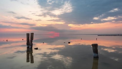 Old wooden pillars in front of Sunset clouds reflected in the smooth water of the lake