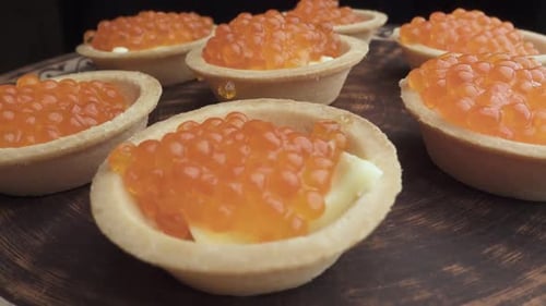 Roter Kaviar wird mit einem Löffel auf Törtchen gelegt. Zubereitung von Snacks mit rotem Kaviar. Ansicht von oben