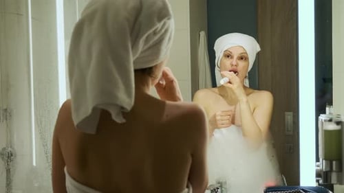 Woman Brushing Teeth in Bathroom Mirror