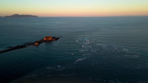 Aerial flyover small waves of Pacific Ocean with outstanding rocks and beautiful colorful sunset at