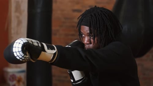Dedicated Young Man Punching Boxing Bag at Gym
