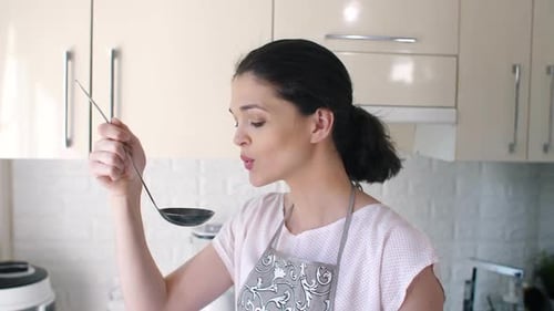 Woman Tasting Food with Ladle in Kitchen