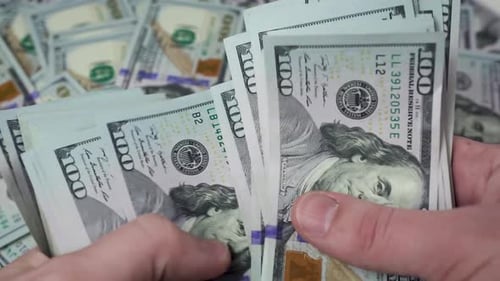 Die Hände eines Mannes zählen einen dicken Stapel Dollar vor dem Hintergrund verstreuter $100-Scheine.